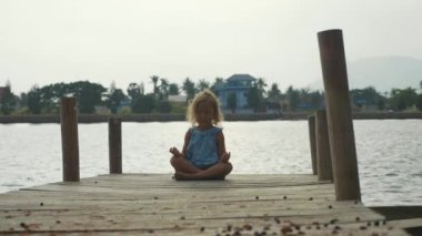 Kız çocuk ahşap iskele lotus poz oturur ve ağır çekimde meditasyon