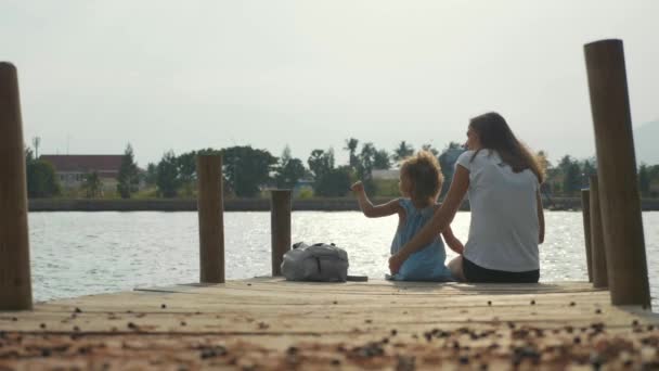 Moeder met kleine dochter zit op de pier en genieten van de natuur in slow motion. — Stockvideo