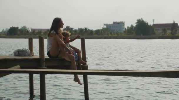 Küçük kızı annesiyle iskelede oturur ve doğa yavaş zevk. — Stok video