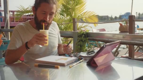 Diseñador masculino dibuja bocetos en la cafetería al aire libre junto al río en cámara lenta . — Vídeo de stock