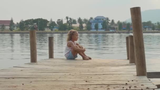 Kind meisje zit op de houten pier en genieten van de natuur in slow motion — Stockvideo