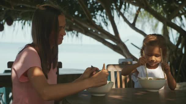 Matka i córka zjada makaron zupa za pomocą pałeczki w kawiarni przy plaży open air — Wideo stockowe