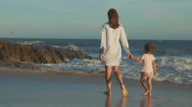 Ağır çekimde holding ile deniz kıyısında yürüyüş bebek annesiyle eller.