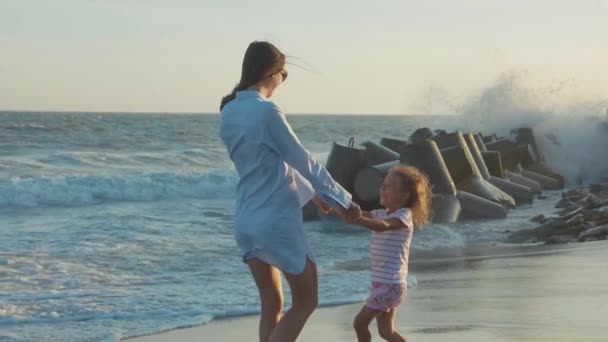 Moeder haar dochtertje aan zandstrand in warm zonsondergang licht spinnen. — Stockvideo