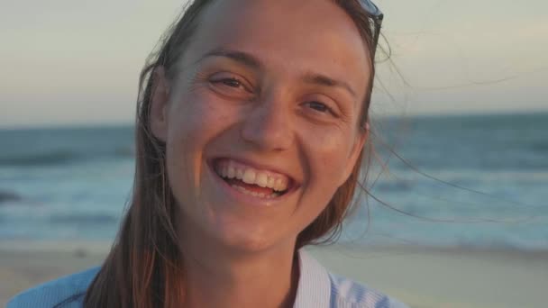 Портрет счастливой женщины, смотрящей в камеру и смеющейся на пляже в замедленной съемке — стоковое видео
