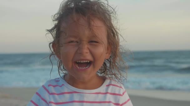 Portrét šťastné dítě holčička při pohledu na fotoaparát a směje se na pláži — Stock video