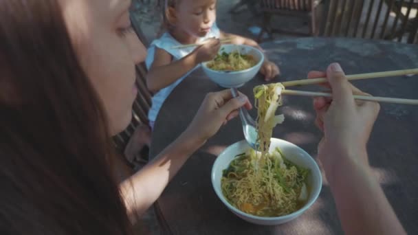 Μητέρα και κόρη τρώει noodles σούπα μέσω Τσοπ στικς στο υπαίθριο beach café — Αρχείο Βίντεο