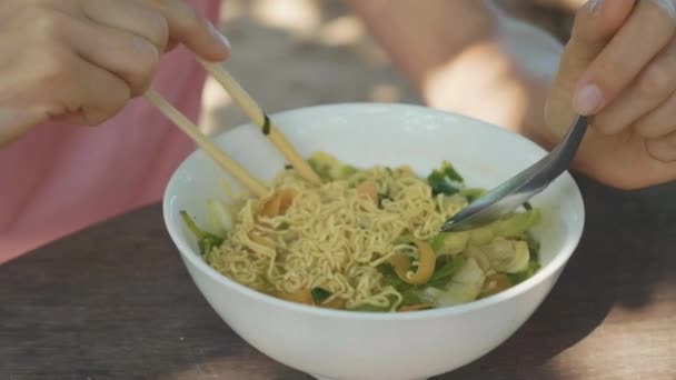 Jonge vrouw eet noodles soep via stokjes in de open lucht strand café — Stockvideo
