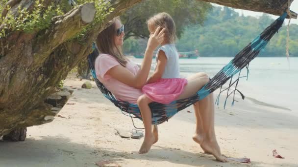 Madre acostada en la hamaca con su pequeña hija linda en la playa de arena — Vídeo de stock