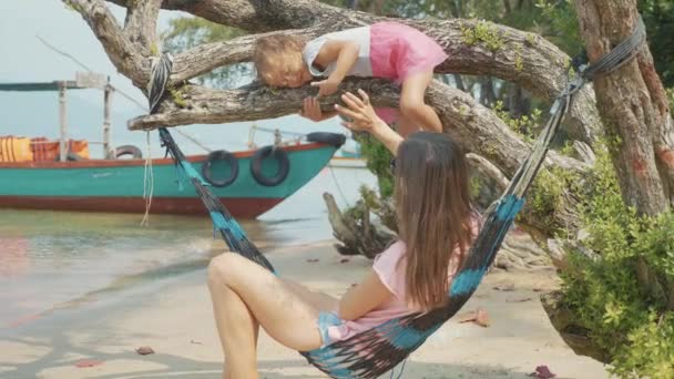 Мама веселится со своей маленькой милой дочкой в гамаке на песчаном пляже — стоковое видео