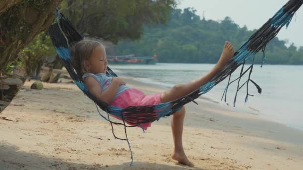 Aranyos gyermek lány függőágyban feküdt és pihenni a homokos tengerparton lassítva — Stock videók