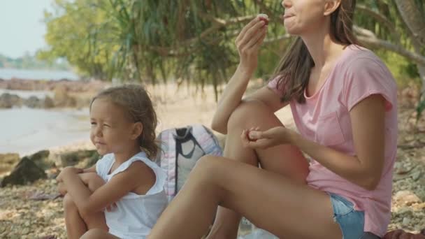 Familie zit op een tropisch strand en eet vruchten in slow motion. — Stockvideo