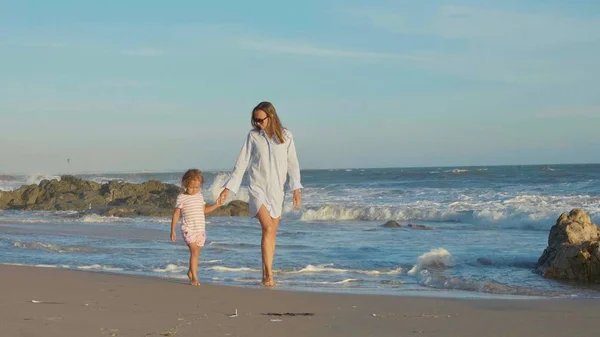 Madre con el bebé caminando en la costa del mar con las manos cogidas . — Foto de Stock