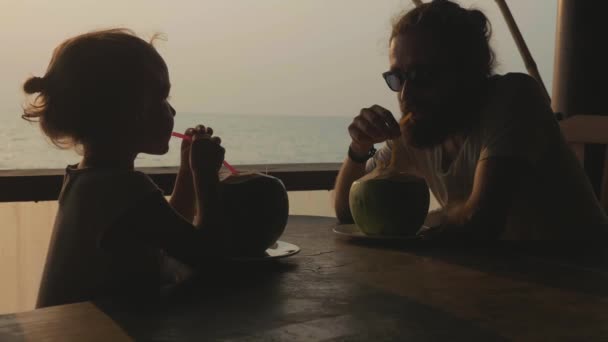 Vater und Tochter sitzen im Meerblick-Café und trinken gemeinsam Mäntel — Stockvideo