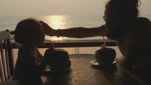 Padre e hija se sientan en la cafetería con vistas al mar y beben cocos juntos — Vídeo de stock