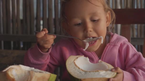 Liten söt flicka äter kokos med sked på café i slow motion — Stockvideo