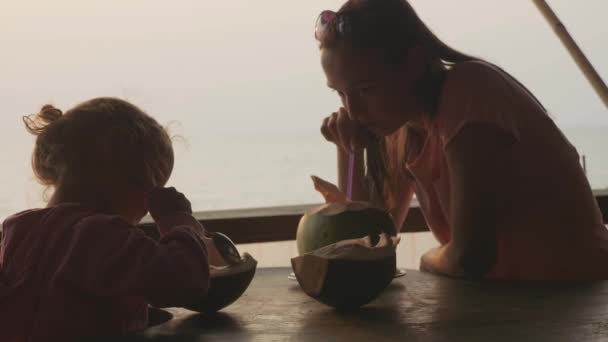 Mother and daughter sits at seaview cafe with coconuts in slow motion — Stock Video