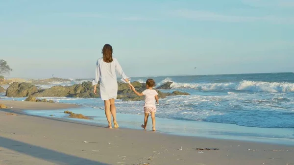 Mãe com bebê andando na costa do mar com as mãos dadas . — Fotografia de Stock