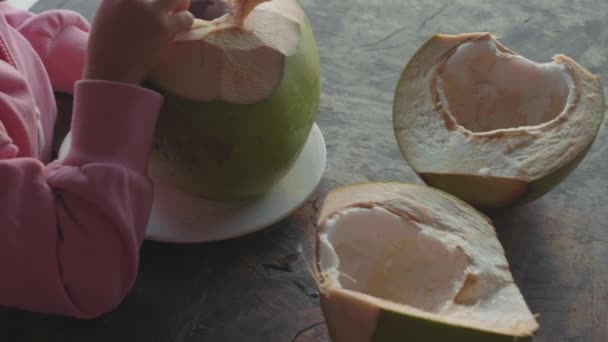 Niña linda comiendo coco por cuchara en la cafetería con vista al mar en cámara lenta — Vídeos de Stock
