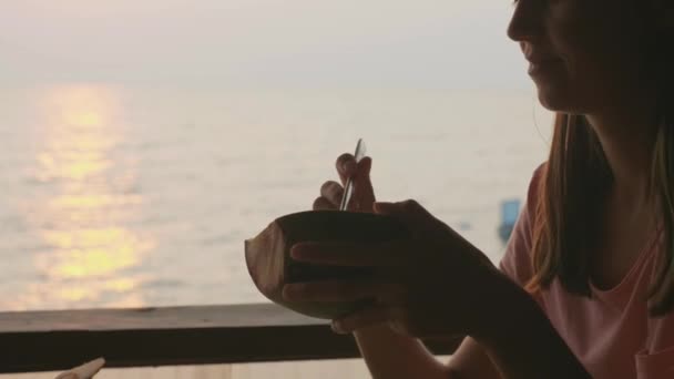 Bambina mangiare cocco da cucchiaio da madri mani al caffè con vista sul mare — Video Stock