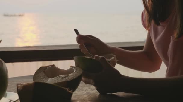Kleines Mädchen isst im Café mit Meerblick Kokosnuss aus den Händen der Mutter — Stockvideo