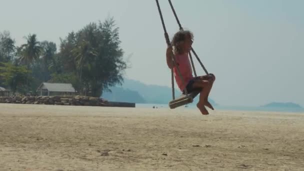 Счастливая смеющаяся девочка, качающаяся на тропическом песчаном пляже со смешными эмоциями — стоковое видео