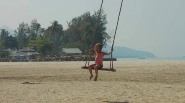 Komik duygular ile tropikal kumlu plajda sallanan mutlu gülen çocuk kız