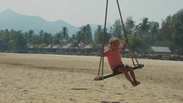 Счастливая смеющаяся девочка, качающаяся на тропическом песчаном пляже со смешными эмоциями — стоковое видео