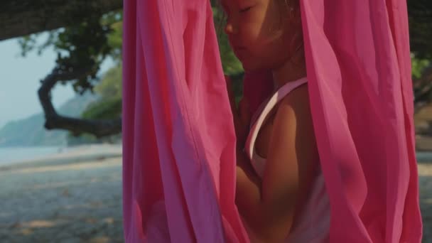 Petite fille mignonne enfant faisant des exercices de yoga avec hamac à la plage . — Video