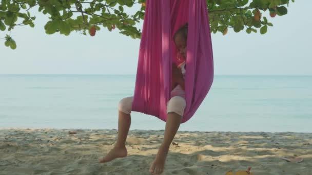 Niña linda haciendo ejercicios de yoga con hamaca en la playa . — Vídeos de Stock