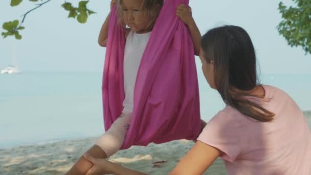 Mor undervisning sitt barn flicka gör yoga favoritapp med hängmatta på stranden. — Stockvideo