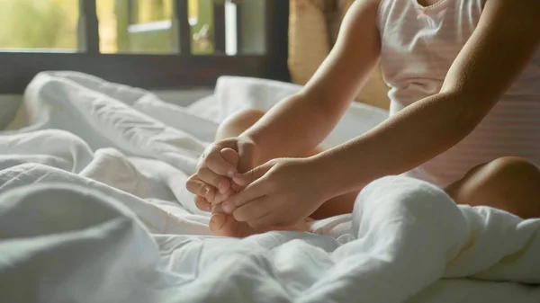 Крупним планом дівчинка сидить на ліжку і грає зі своєю ногою — стокове фото