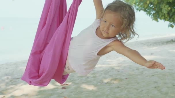 Liten söt barn flicka gör yoga favoritapp med hängmatta på stranden. — Stockvideo