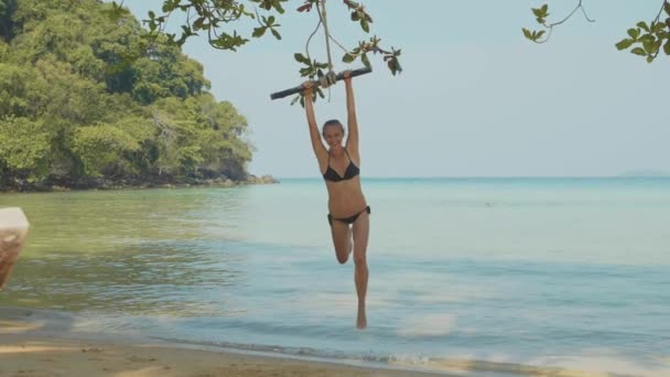 Happy young woman swinging on rope at beautiful beach — Stock Video