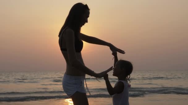Silueta de madre joven con hija pequeña bailando en la playa al atardecer — Vídeo de stock