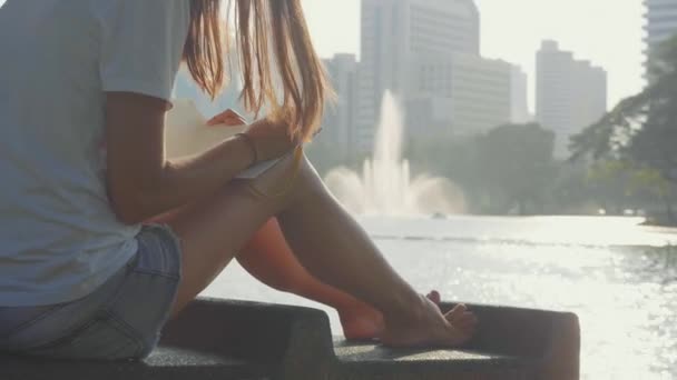 Jovem mulher sentada no banco no parque e escrevendo em diário, close-up — Vídeo de Stock