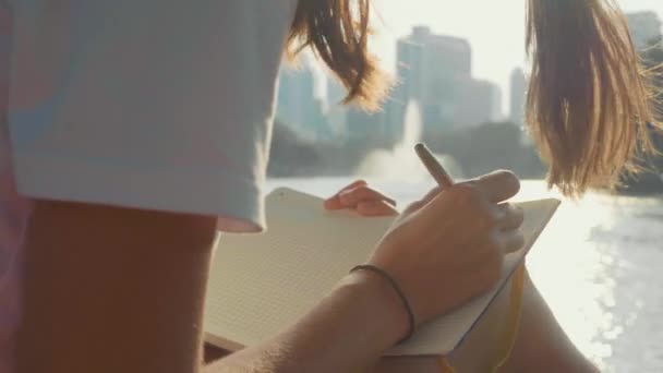 Mujer joven sentada en el banco en el parque y escribiendo en el diario, primer plano — Vídeos de Stock