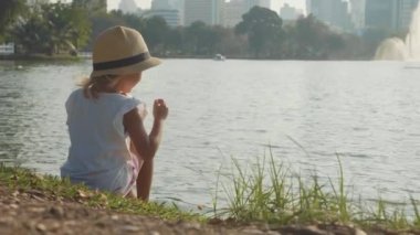 Yavaş çekimde bir park gölde balık besleme ülke stil şapkalı küçük kız