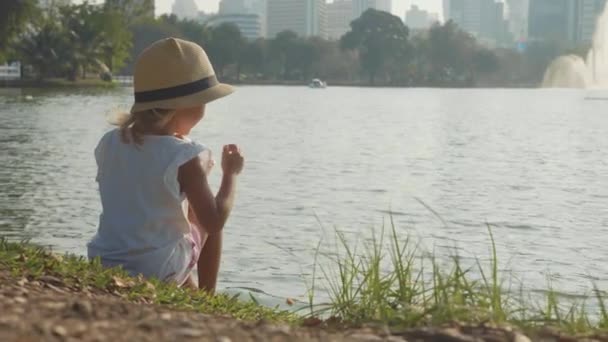 Niña en el estilo de país sombrero de alimentación de peces en un lago parque en cámara lenta — Vídeos de Stock