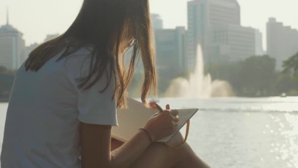 Mujer joven sentada en el banco en el parque y escribiendo en el diario, primer plano — Vídeo de stock