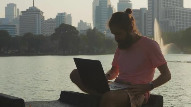 Homem barbudo abrindo laptop e começar a trabalhar no banco no parque da cidade de megapolis — Vídeo de Stock