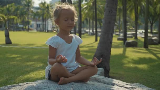 Meisje kind mediteren in prachtig park met palmbomen op de achtergrond — Stockvideo