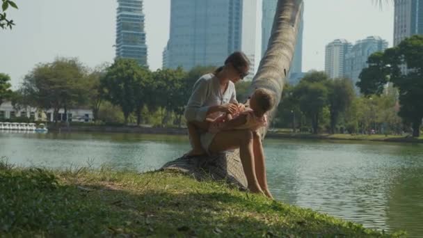 Familia divirtiéndose en el parque con lago y rascacielos en el fondo — Vídeos de Stock