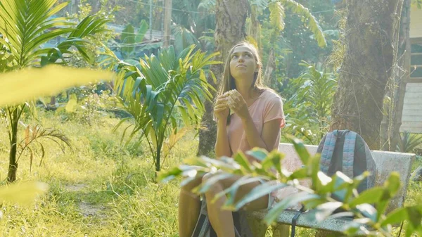 Jovem mulher sentada no banco na aldeia rural asiática e comer lanche — Fotografia de Stock