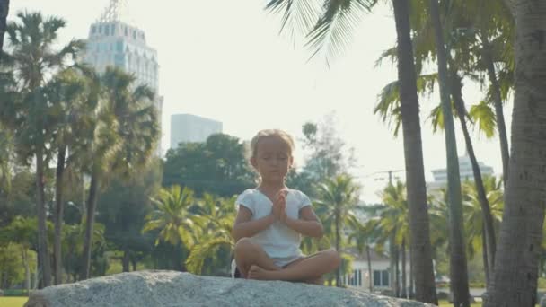 Niña meditando en hermoso parque con palmeras en el fondo — Vídeo de stock