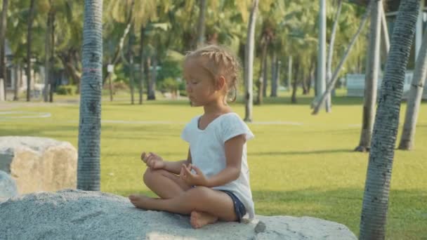 Niña meditando en hermoso parque con palmeras en el fondo — Vídeos de Stock