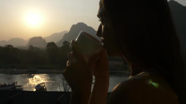 Молода жінка п'є гарячу каву на балконі з красивим гірським пейзажем — стокове відео
