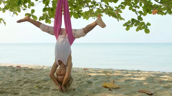 Niña linda haciendo ejercicios de yoga con hamaca en la playa — Foto de Stock