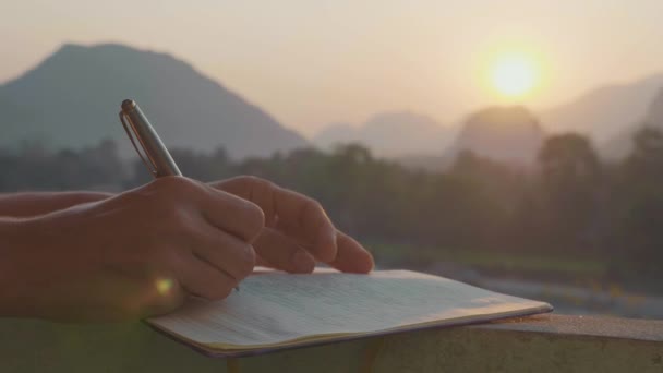 Молодая женщина пишет утренние страницы в дневнике на открытом воздухе, крупным планом в замедленной съемке — стоковое видео
