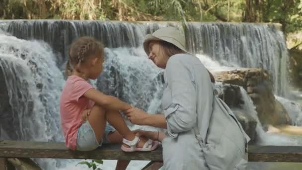 Eine junge Mutter und ihre süße Tochter ruhen sich an einem Wasserfall aus — Stockvideo